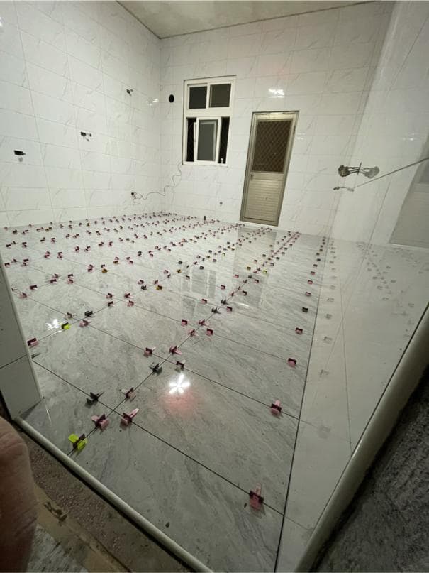 1) 照片顯示一個正在裝修的浴室,地板鋪設了白色的磁磚,牆壁上也是白色的磁磚