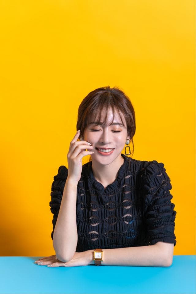 這張照片是一個微笑的年輕女子,她坐在藍色桌子上,戴著金色的手錶。