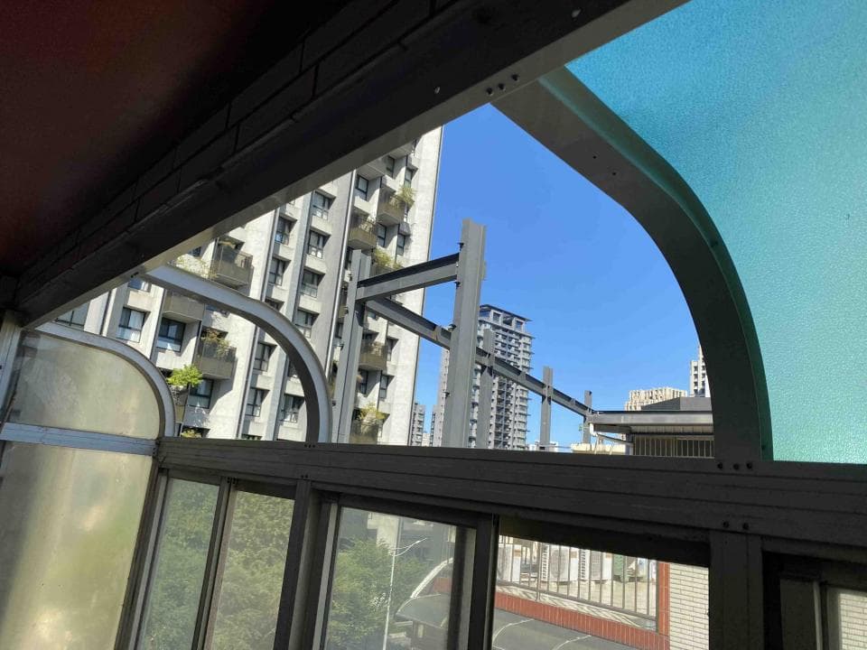 1) 照片顯示一個建築物從陽台往外看出去的景色,陽台是弧形的,覆蓋著透明的屋頂,可以看到許多高樓,也有一些植栽