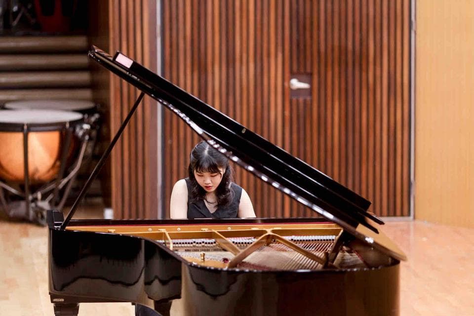 這張「鋼琴演奏」的照片是一名女性音樂家坐在鋼琴前,準備演奏。她穿著黑色衣服,看起來專注而優雅。背景是木質的牆壁,襯托出鋼琴的黑色光澤。