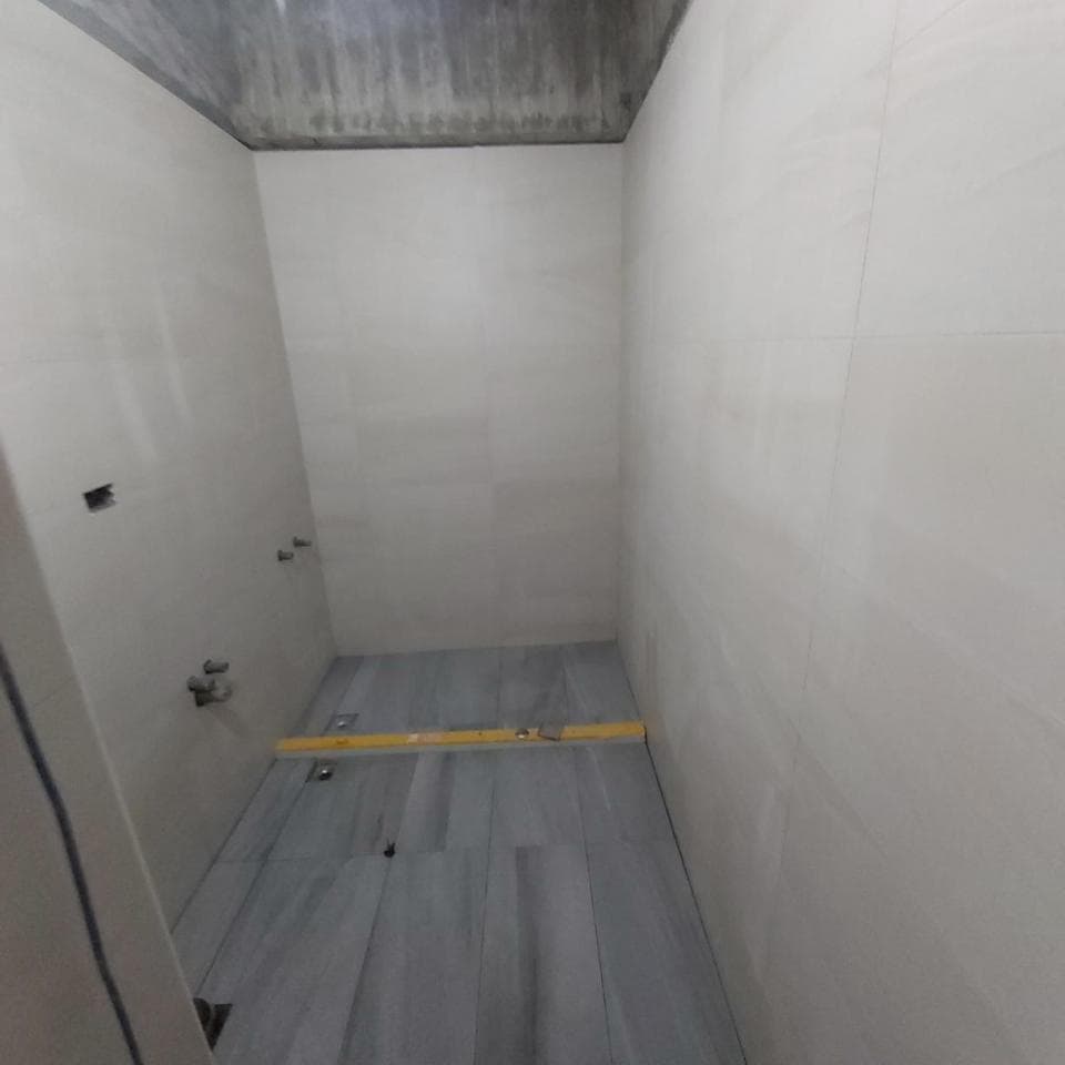 1) 照片顯示一個空浴室,浴室正在裝修,牆壁都已貼上磁磚,地板也鋪好了,牆壁是白色磁磚,地板是灰色磁磚,看起來像是剛完成的浴室