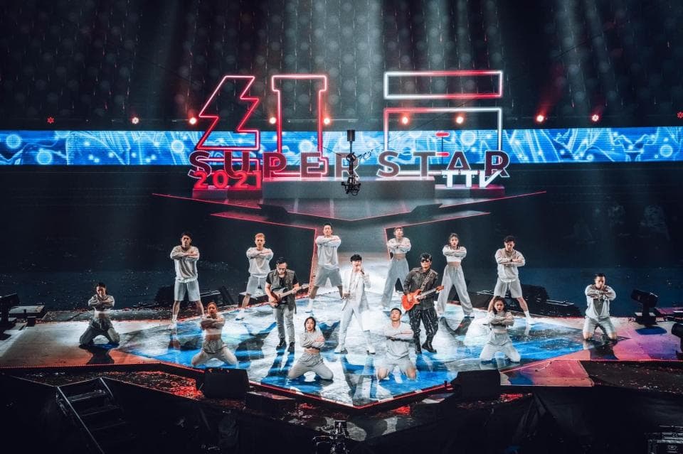 1) 照片顯示了一群人在舞台上表演,舞台上擺著「超級巨星 2021」的標語