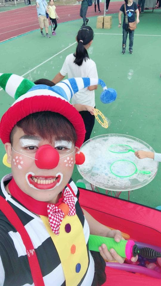 1. 照片顯示一位穿著小丑服裝的男子,他戴著紅色的假髮、鼻子和化妝,他拿著一個泡泡棒,笑容滿面