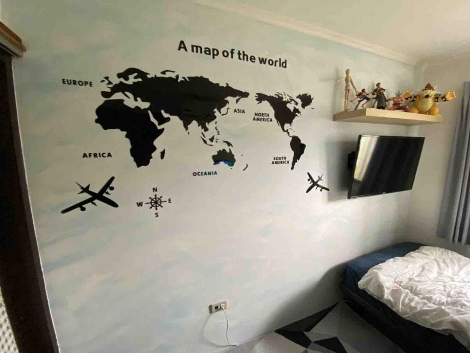 1) 照片顯示一個房間的一角,牆上貼著世界地圖,地圖周圍有飛機和指南針的貼紙,牆上還掛著電視,房間裡還有一張床和一些裝飾品