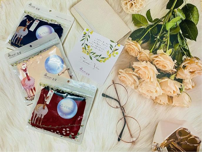 這張「包裝好的布料」的照片是三種不同圖案的布料,分別是藍色、粉色和紅色,每個布料都印有可愛的小鹿圖案。 旁邊有一束淡粉色的玫瑰花,襯託布料的柔美。