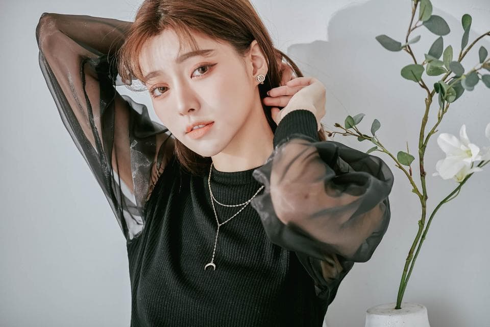 這張「女性肖像」的照片是一個穿著黑色透視上衣的女孩,她戴著項鍊和耳環,背景是一株白色花卉植物。