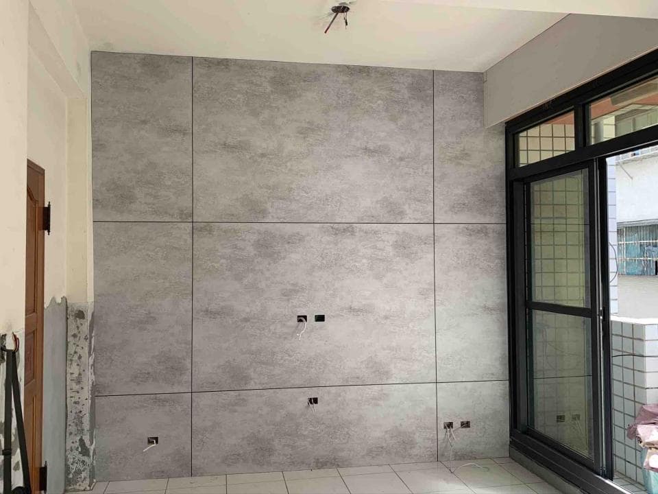 1) 照片顯示一個房間角落,牆壁上裝潢了仿水泥的裝飾板,房間角落有一扇落地窗,窗戶外有陽台