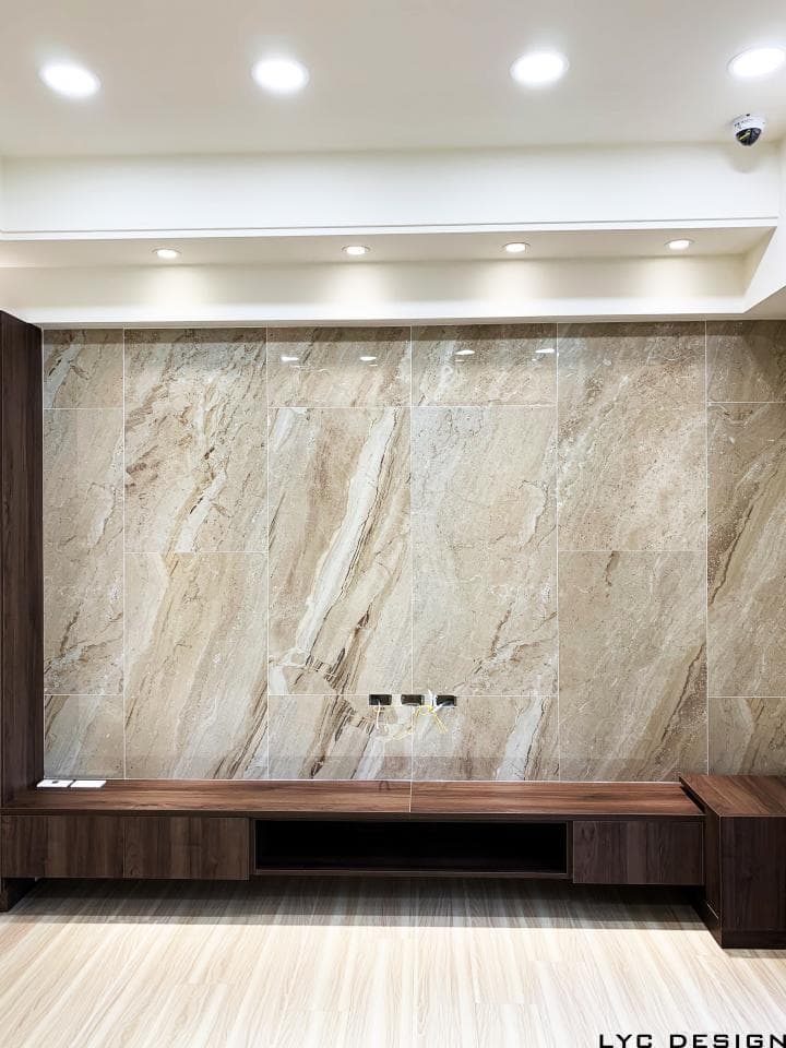 這張照片是一間現代化的客廳,最顯眼的元素是牆上的米色大理石磚,搭配深色木質電視櫃,展現出簡約又不失質感的空間設計。