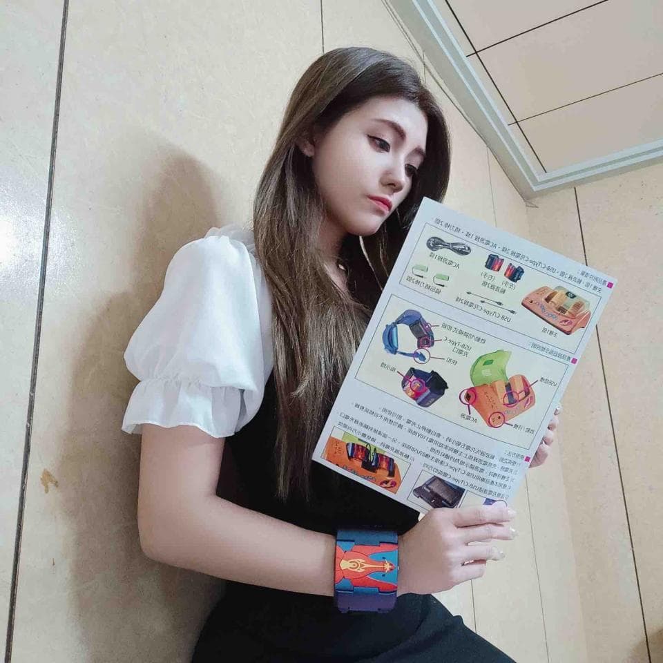 1) 照片中是一位年輕女性,穿著白色上衣和黑色裙子,她拿著一本中文說明書,手戴著一個彩色手環,並看著鏡頭