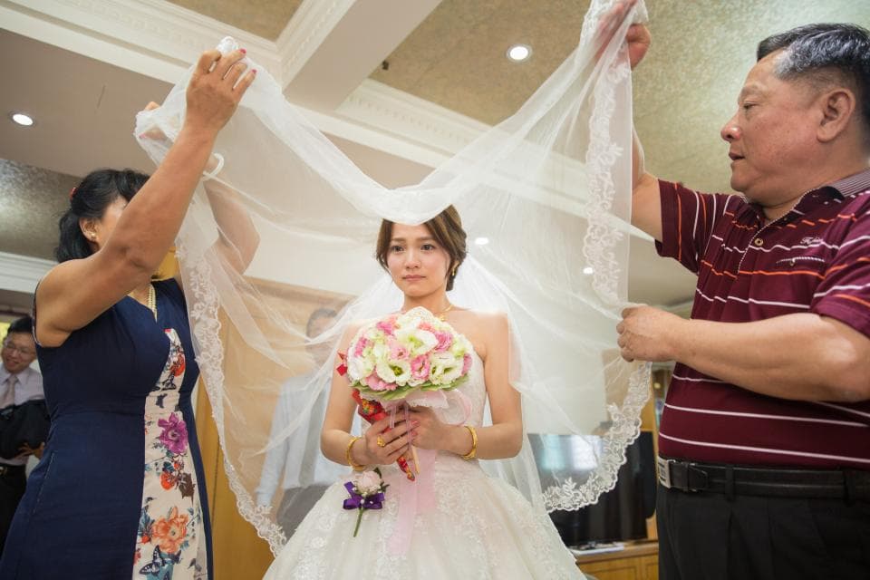 這張照片是一個婚禮的場景,新郎正在幫新娘蓋頭紗。