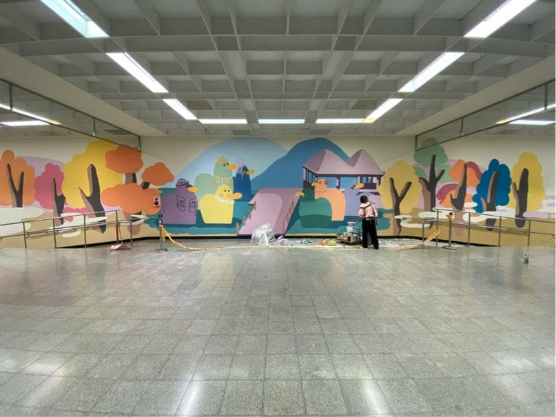 這張「地下通道」的照片是一幅帶有童趣的壁畫,牆壁上繪有可愛的卡通人物、樹木和房屋,整體氛圍明亮歡快,令人感到輕鬆愉悅。