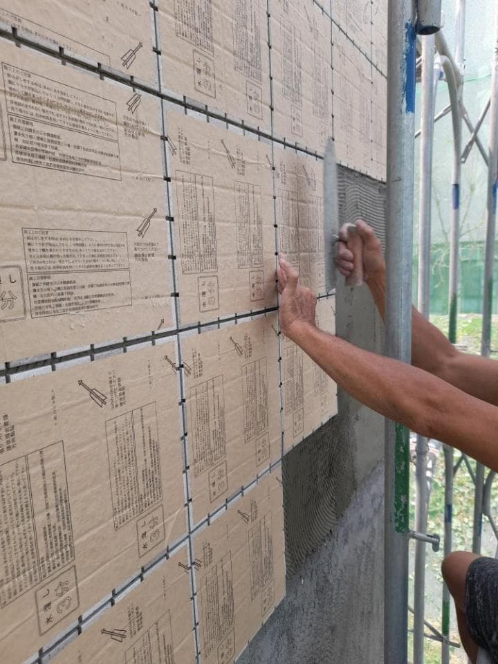 1) 照片顯示一名工人正在將瓷磚貼到牆上,牆上已貼滿瓷磚