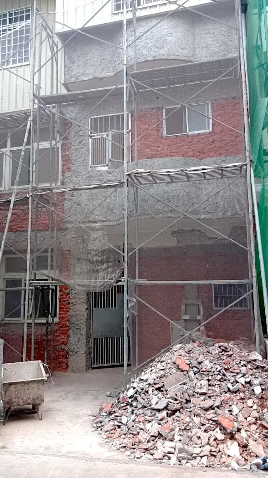 這張照片是一棟正在進行整修的建築物,建築物外圍架設了鷹架,周圍也堆放著許多建築廢棄物。