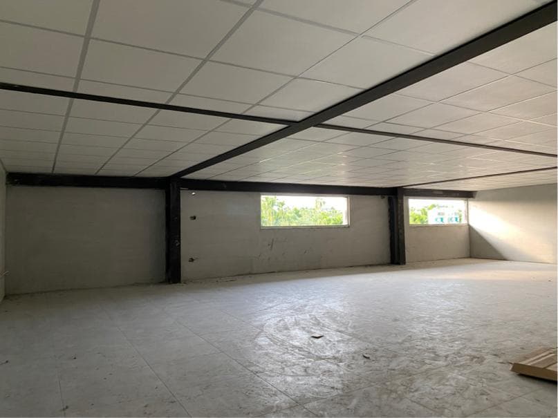 1) 照片顯示了一個大型空房間,房間的牆壁是白色的,天花板上有黑色的橫樑,房間裡有兩個窗戶,可以看到外面的樹木