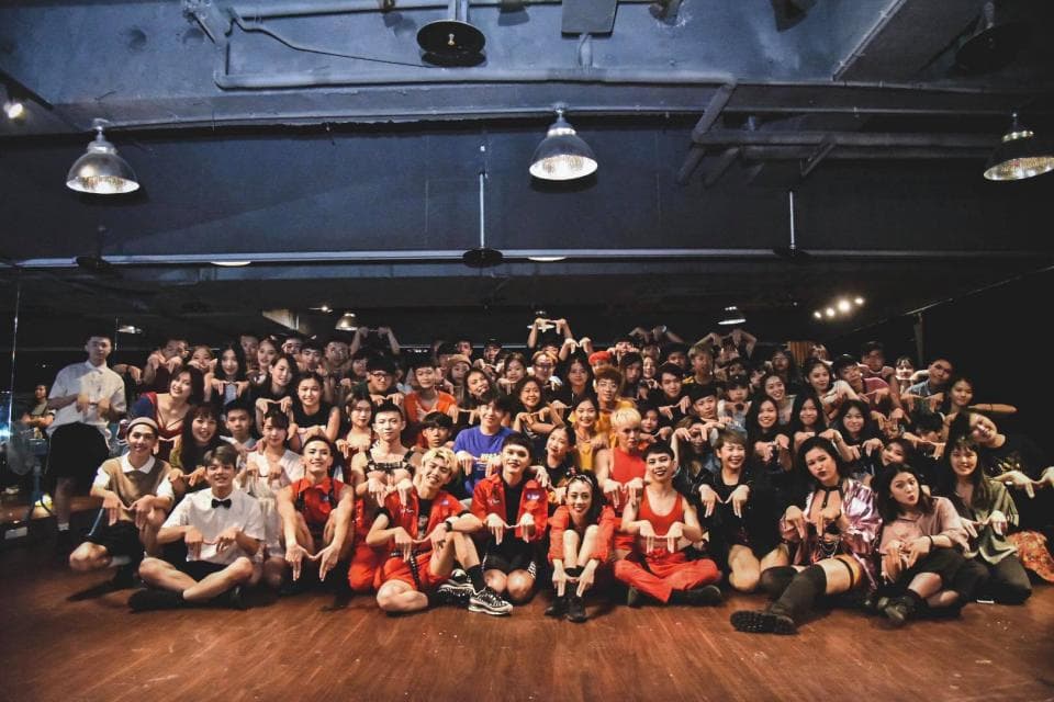 這張照片是一群人圍成一個圈,在一個室內空間裡擺出姿勢,他們笑容滿面,看起來很開心。