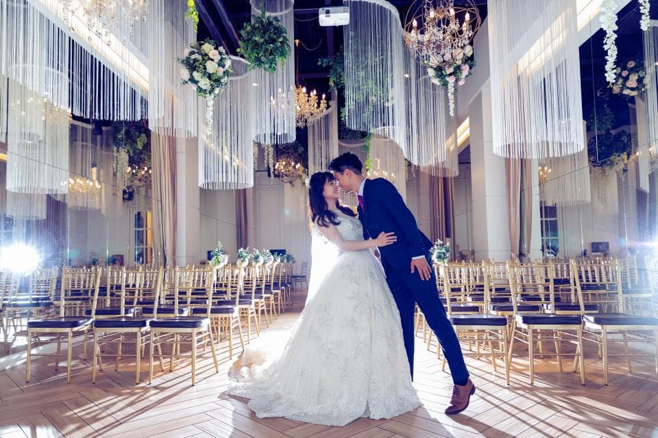 這張照片是新郎新娘在婚禮上深情擁吻,背景是佈置精美的婚禮場地,營造出浪漫溫馨的氛圍。