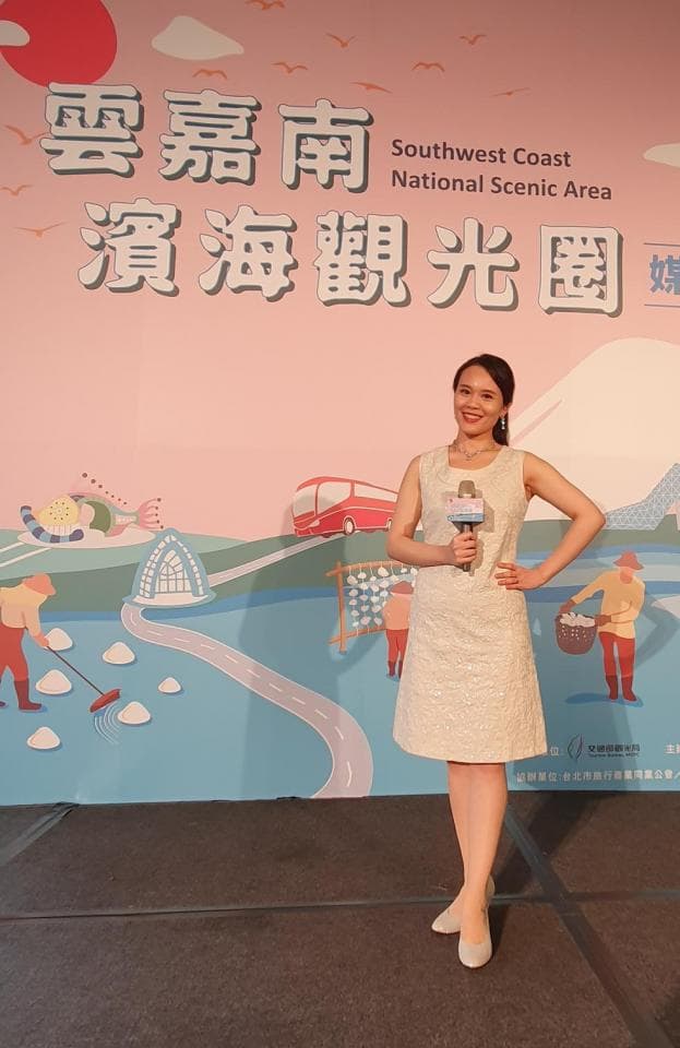 這張「西南海岸國家風景區」的照片是一位女性站在舞臺上,背景是風景區的介紹圖,她手持麥克風,身穿白色蕾絲洋裝。