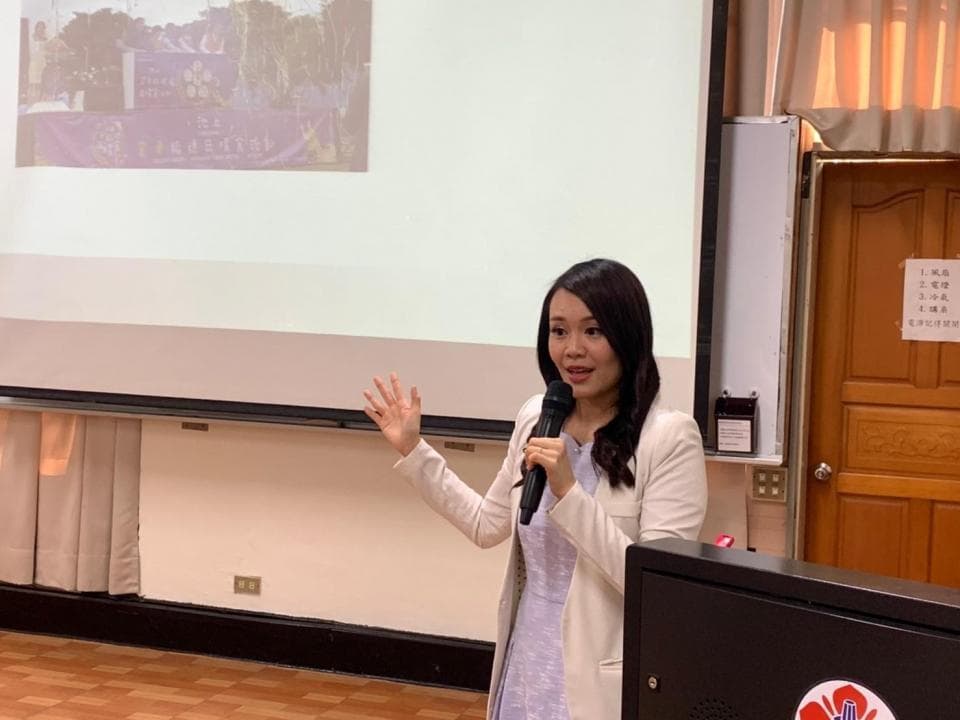 這張「女性演講」的照片是,一位女性站在投影機前,拿著麥克風,正在演講。