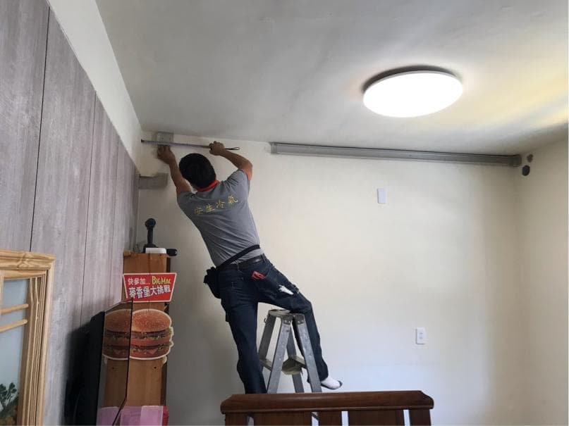 1) 照片顯示一名男性站在梯子上,正在安裝天花板燈