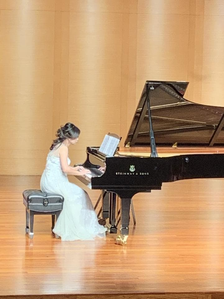 這張「鋼琴演奏」的照片是一個穿著白色禮服的女生坐在一臺黑色的鋼琴前演奏。