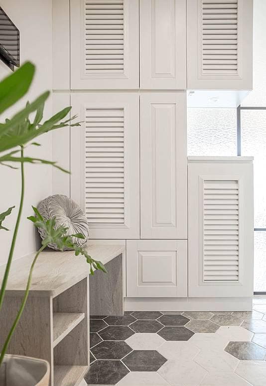 1) 這是一張室內設計的照片,展示了帶有百葉窗的白色櫥櫃、一個木頭長凳、一個灰色靠墊和一個六角形瓷磚地板