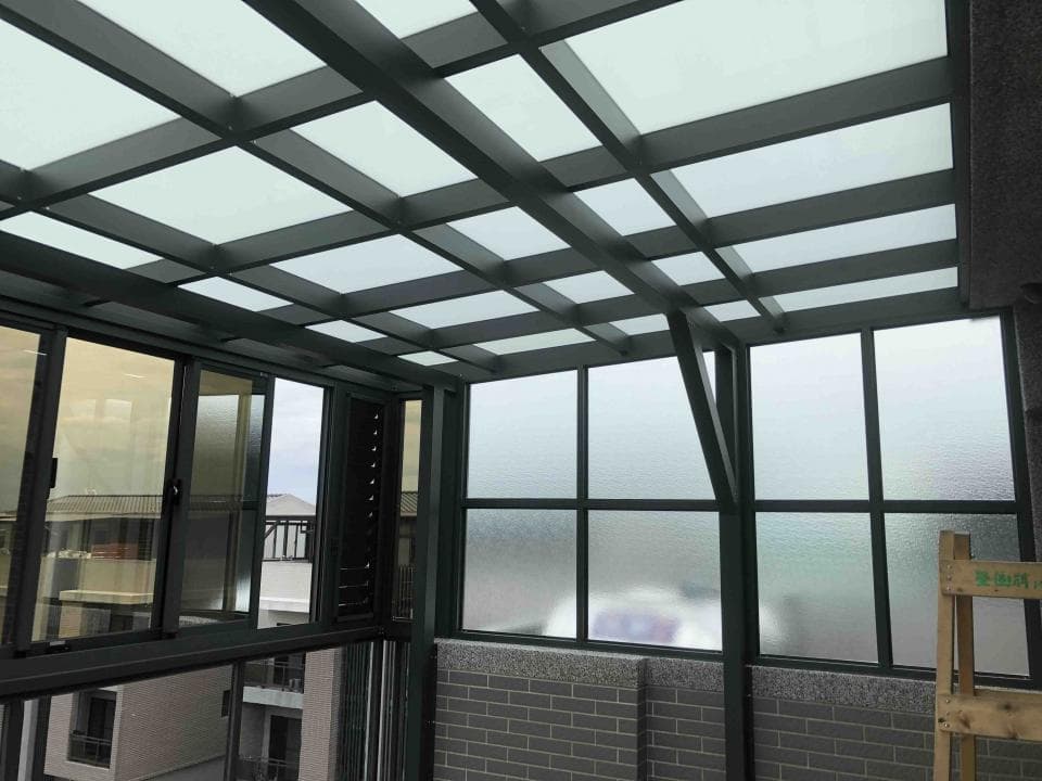 這張照片是一個現代化的玻璃屋頂,由黑色鋼架支撐,並用透明玻璃板覆蓋。透過玻璃可以看到外面的景色,非常明亮通透。