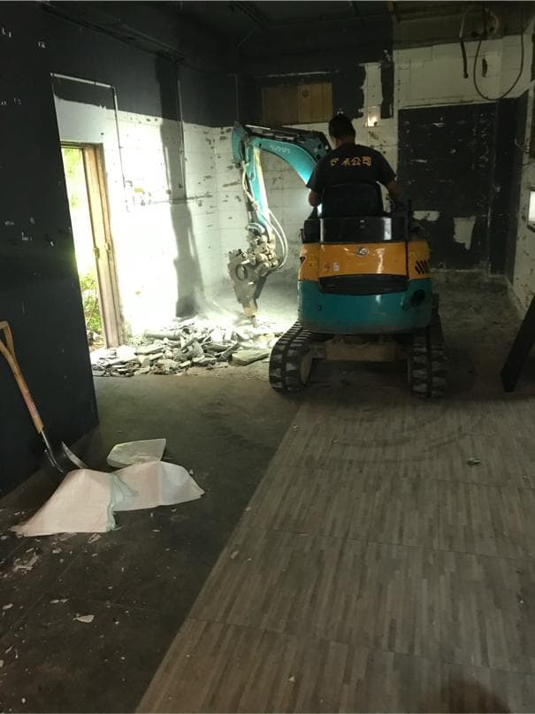 1) 照片顯示一個正在拆除建築物的房間,房間裡有一台小型挖掘機,房間裡還有一個人在操作挖掘機