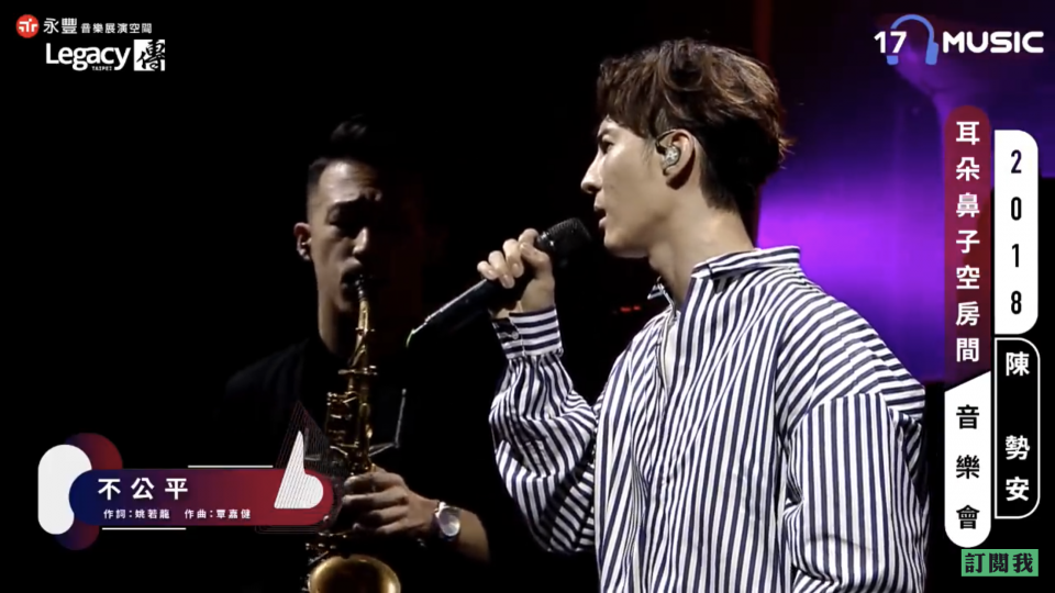 這張「歌手在舞臺上唱歌」的照片是,一位歌手穿著條紋襯衫,手拿麥克風唱歌,他身後有一位演奏薩克斯風的樂手。