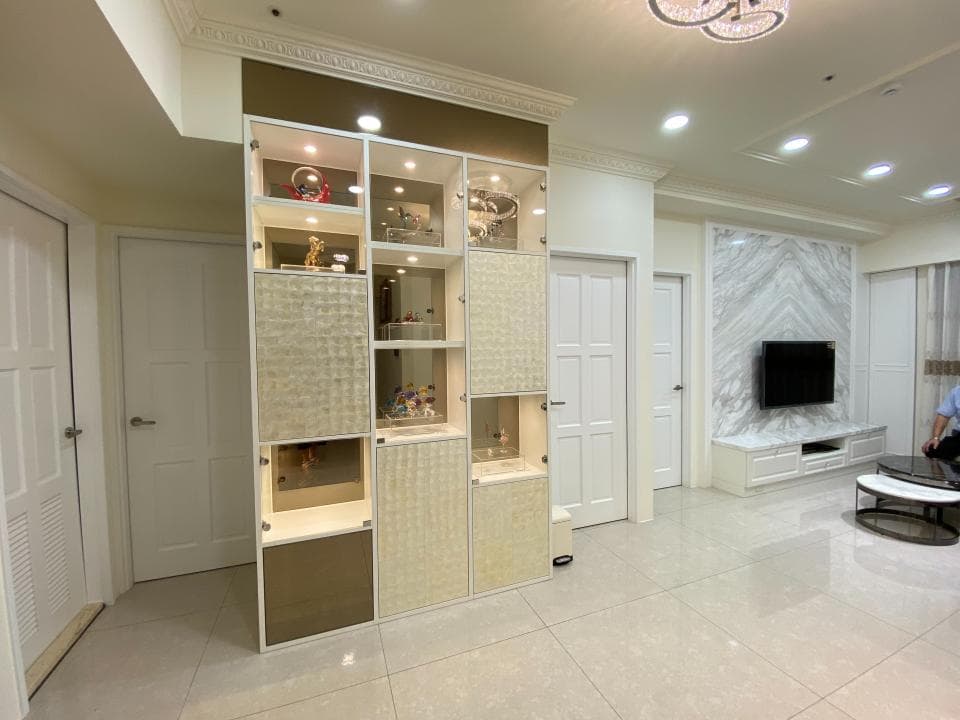 這張照片是一個現代化的客廳,房間中央放著一個大型的白色櫃子,櫃子分層擺放著許多裝飾品,看起來非常時尚。