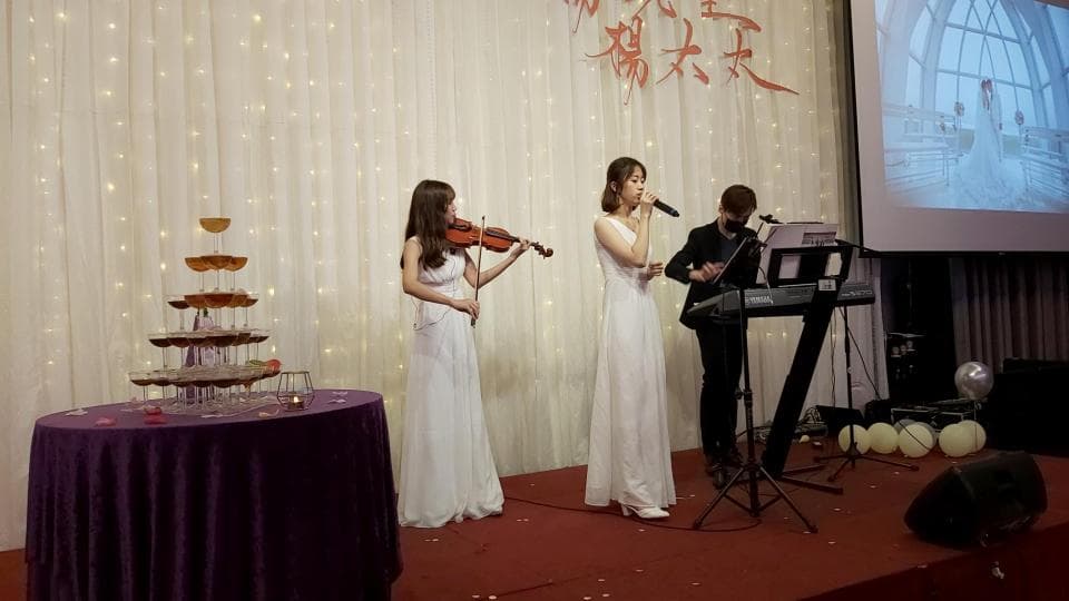 這張婚禮的照片是一個婚禮現場的樂隊,一個女孩在演奏小提琴,另一個女孩在唱歌,一個男生在彈鋼琴。