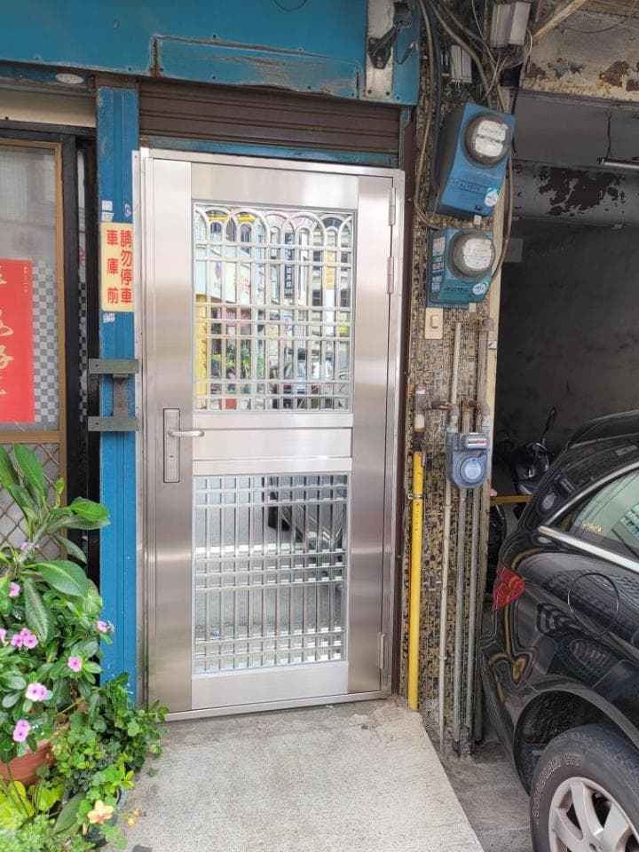 1) 這是一張照片,展示了一扇金屬門,門上裝有玻璃窗格,門的旁邊有一面牆,牆上有一些電器設備,牆的右邊有一輛黑色汽車