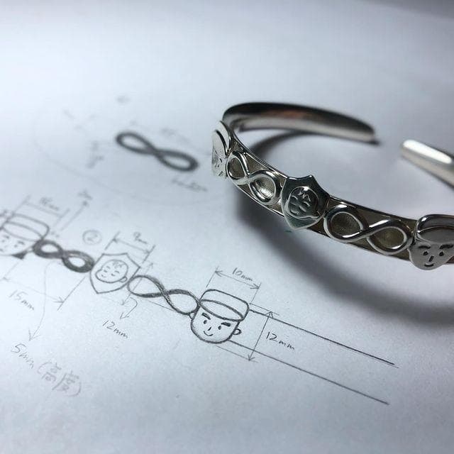 這張照片是一條銀色的手鐲,手鐲上刻有無限符號和一個戴帽子的卡通人物。