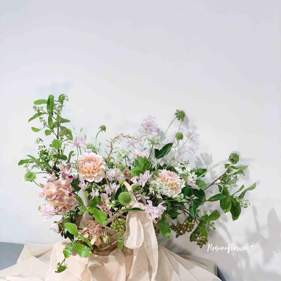 這張照片是一束美麗的花,有粉色和白色花朵,以及綠色的葉子,它們被安排在一個籃子裡,並被一條粉紅色的緞帶裝飾。