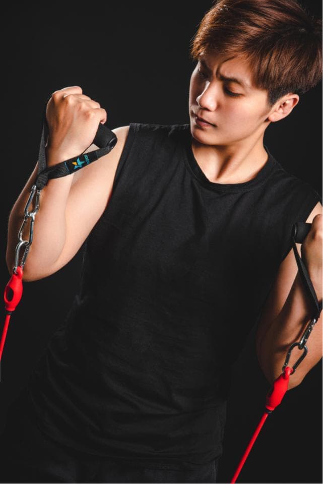 這張照片是一個年輕人正在使用阻力帶運動,他專注地看著自己的手臂,並認真地進行鍛鍊。