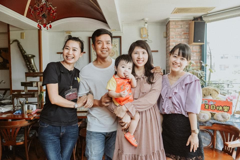 這張照片是四位朋友在一家餐廳聚會,其中一位懷抱著一個可愛的小男孩,他們看起來很開心,享受著美好的時光。