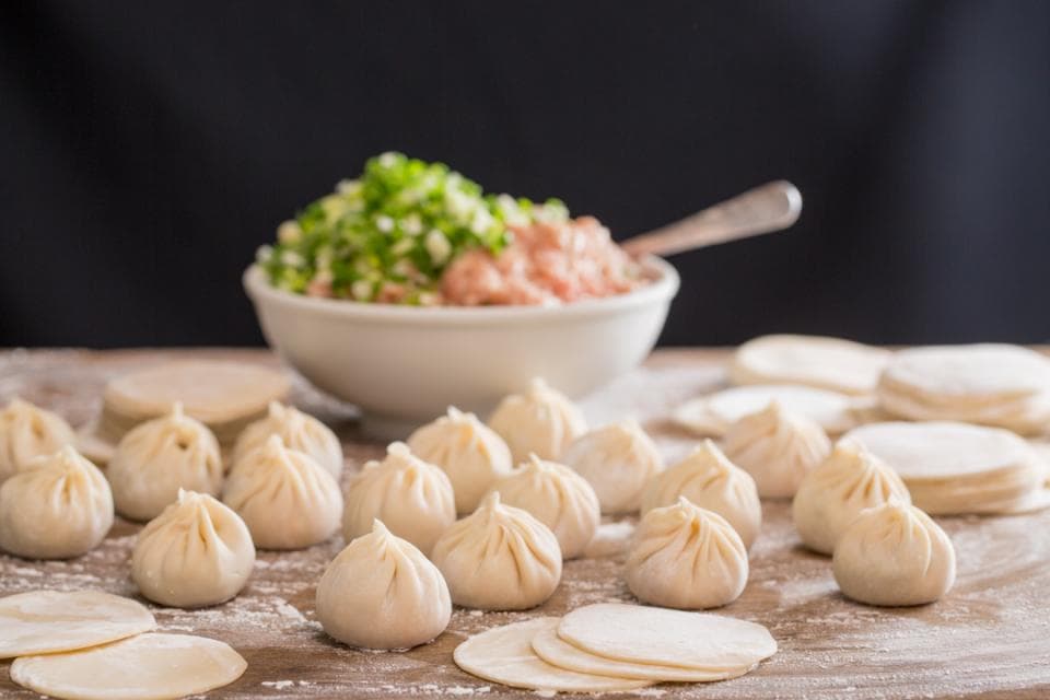 這張「餃子」的照片是很多個包好的餃子,放在木桌上,旁邊有餡料,還有碗盤。