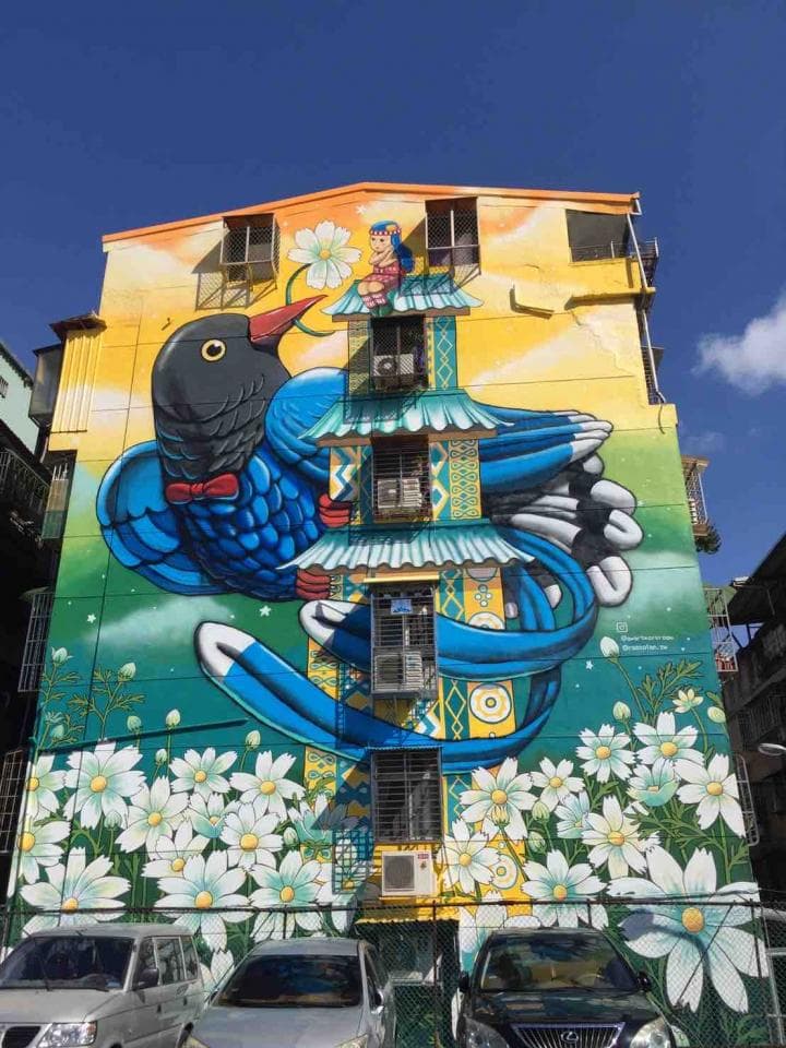 這張「彩繪牆」的照片是藍色鳥和女孩,背景是黃色的牆壁和白色花朵。