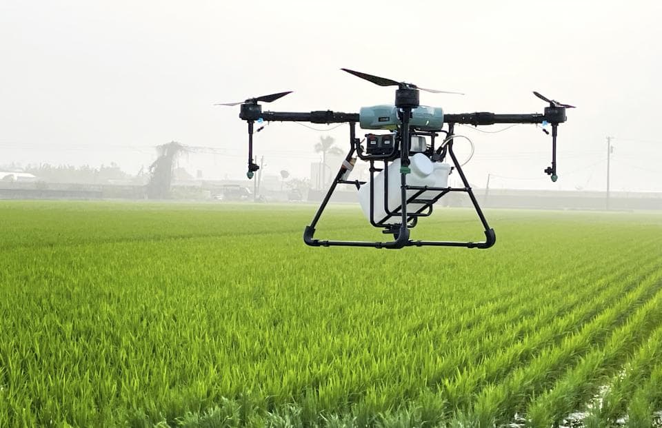 這張照片是一架無人機在稻田上空噴灑農藥。無人機配備了噴灑系統,可以將農藥精確地噴灑到稻田上。無人機的噴灑系統可以減少農藥的使用量,並提高農藥的效率。