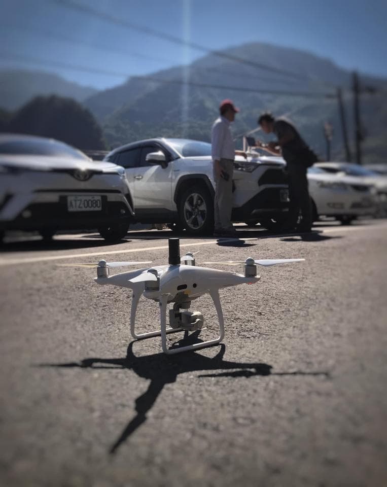 這張照片是一架白色無人機停放在柏油路面上,無人機的下方投射出巨大的陰影,顯得格外顯眼。