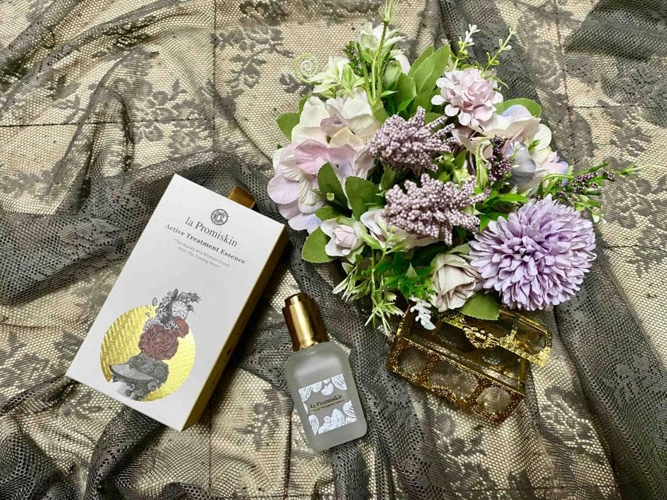 這張照片是一瓶精華液,包裝精美,瓶身透明,可以清楚看到液體的顏色。瓶子旁邊有一朵紫色的花,花瓣柔軟,顏色淡雅。