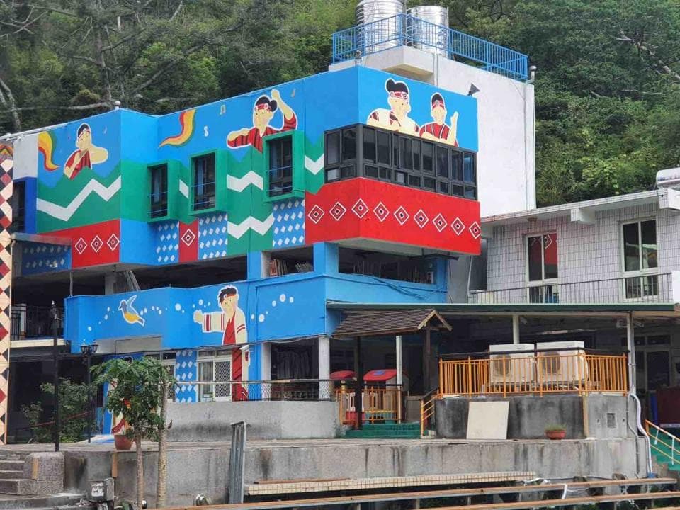 這張照片是一個以紅色和藍色為主題的建築,上面繪有許多人物圖案,牆壁上也充滿了各式各樣的圖案。建築物看起來很新,而且很明亮,周圍種植了許多綠色植物,令人感覺很舒適。