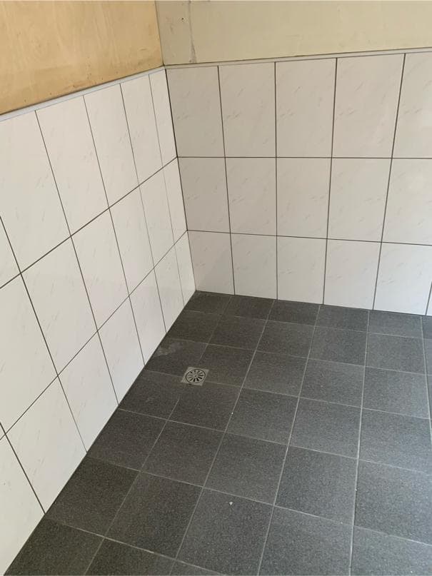 1) 這張照片顯示一個角落的浴室,牆壁上鋪著白色瓷磚,地板上鋪著灰色瓷磚