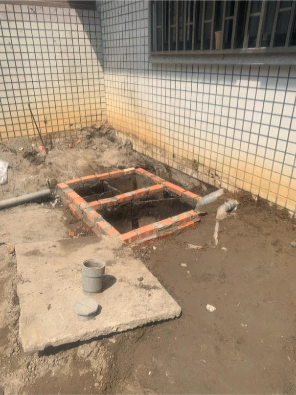 這張照片是一個正在建造的地下室。照片的重點是地下室的磚砌結構,以及地上的一個水泥蓋。地下室的磚砌結構呈現出一個矩形的形状,底部有一個方形的開口。水泥蓋是用來覆蓋地下室的開口,防止灰塵和其他雜物掉進去。