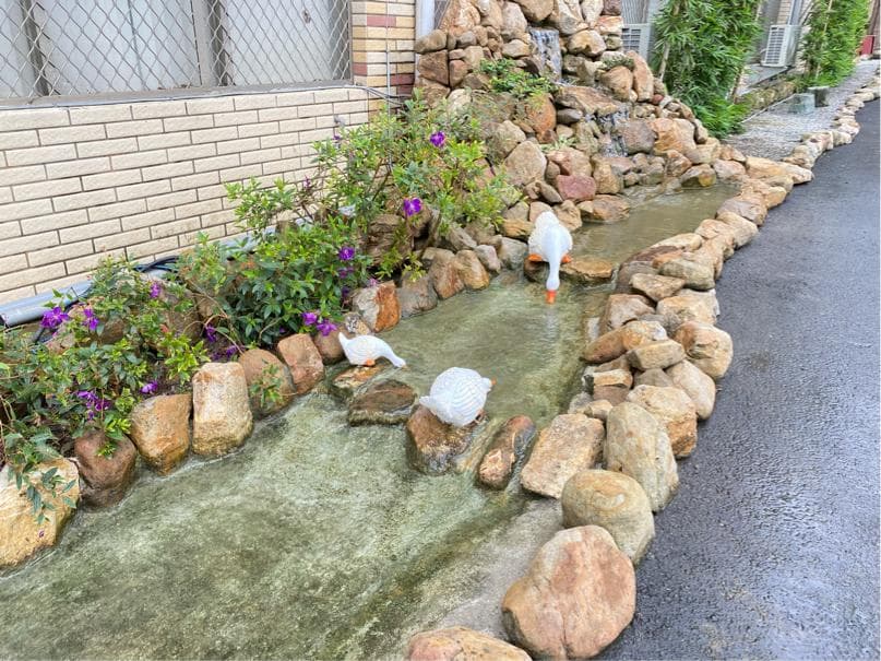 這張照片是一個庭院,有石頭、流水和幾隻白色的鴨子。