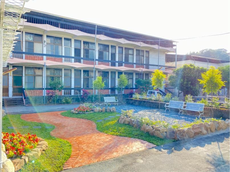 這張照片是一棟現代建築,建築外有花園和步道,花園裡種植了綠草和鮮花,步道以紅磚鋪成,呈現出自然與現代的融合之美。