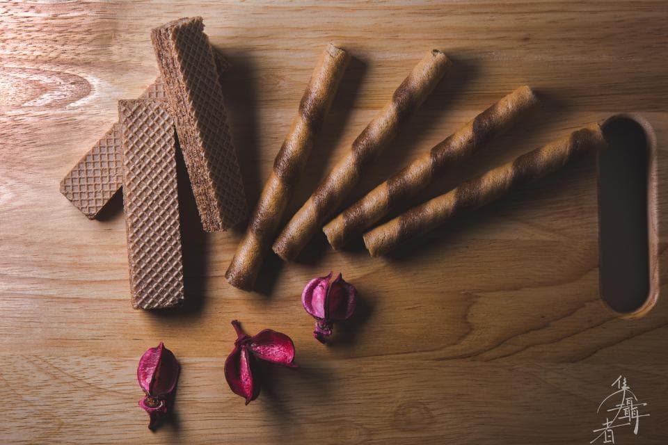 這張「點心」的照片是幾根巧克力威化餅乾放在木板上,旁邊還有幾朵乾燥花。