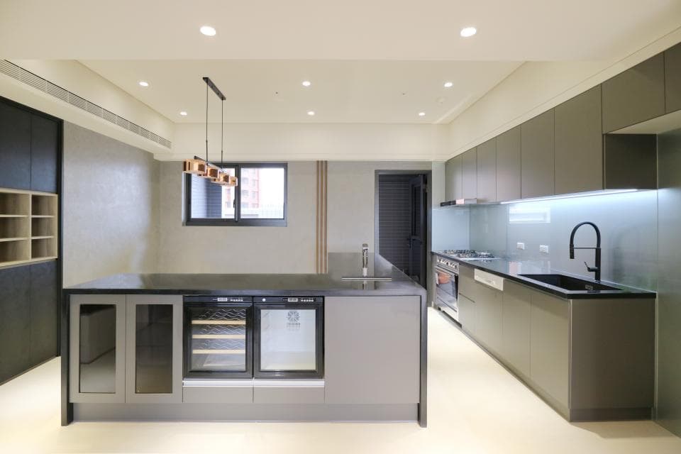 這張照片是一間現代化的廚房,最顯眼的是中間的黑色中島,上面有嵌入式的酒櫃和冰箱,讓整個廚房空間顯得更高級和實用。