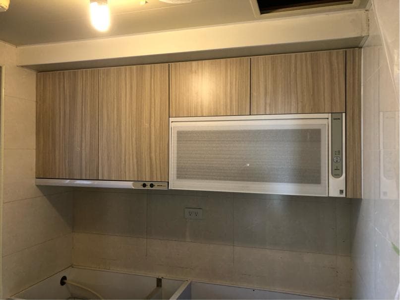 這張照片是一間廚房,最顯眼的是牆上的木紋櫥櫃和嵌入式微波爐,整體感覺簡潔明亮。