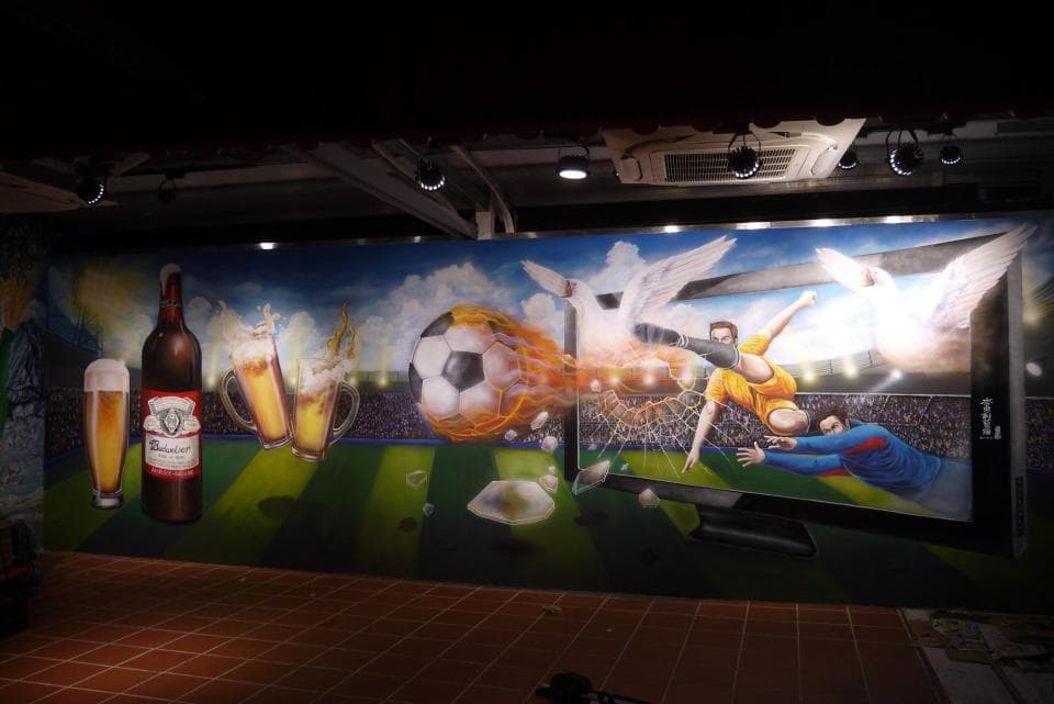 這張「足球場」的照片是描繪一個足球比賽的場景,足球員正在射門,場邊也有觀眾,還有啤酒和足球的塗鴉。