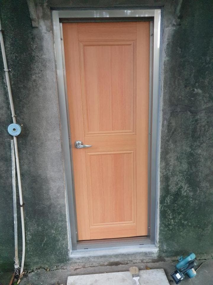 1) 照片顯示一扇木製的門,門框為鋁製,門上有把手,門外有水泥牆,牆上有兩個灰色的水管